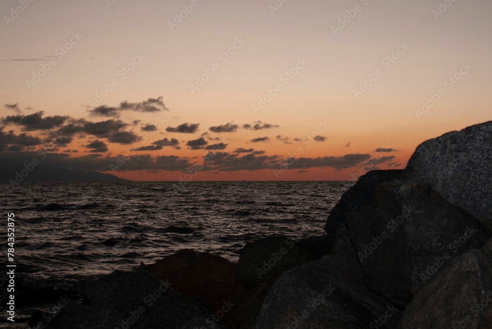 Red sunset view over a seascape with clear sky and sun in the background stones silhouettes around