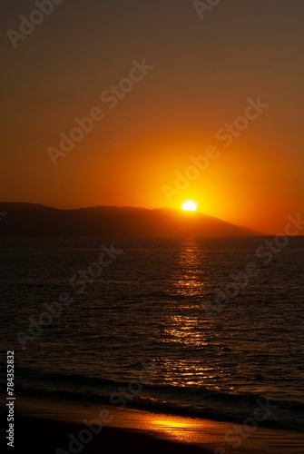 Red sunset view over a seascape with clear sky and sun in the background stones silhouettes around © Wirestock