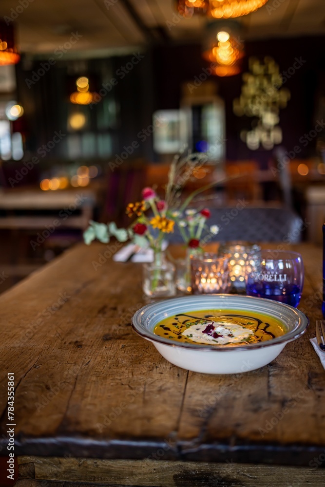 Vertical shot of Pumpkin soup served in a bowl on a wooden table in a cafe