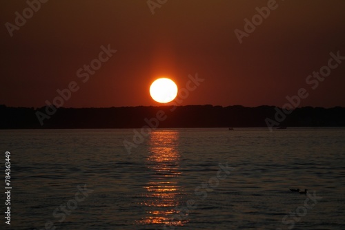 Scenic view of sunset over a calm coast and island © Wirestock