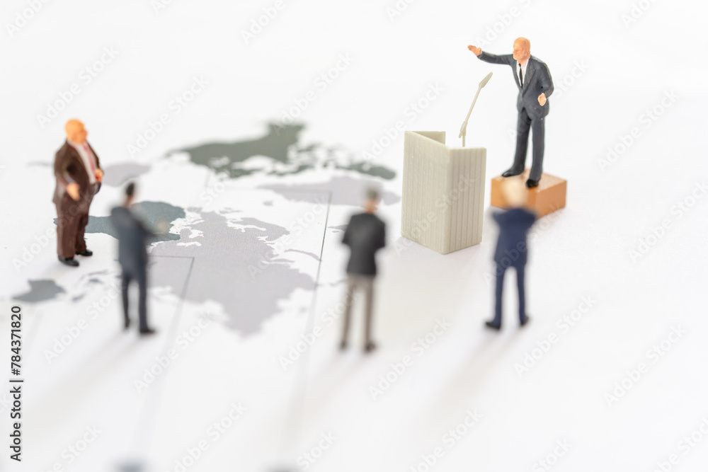 Miniature people: Miniature figurine of a politician speaking to the people during an election rally or an executive speaking to the shareholders on world map Miniature people: Miniature figurine of a politician speaking to the people during an election rally or an executive speaking to the shareholders on world map