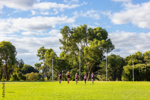 five children running away towards goal posts on football oval photo