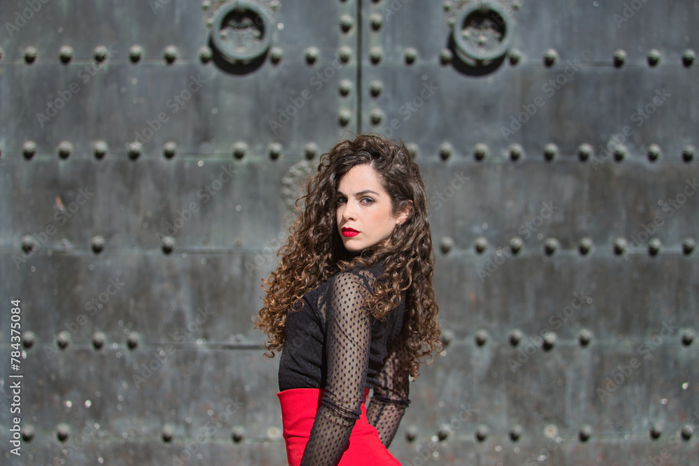 Portrait of young, beautiful, brunette woman in black shirt and red skirt, dancing flamenco with old, black metal door in the background. Flamenco concept, dance, art, typical Spanish. Portrait of young, beautiful, brunette woman in black shirt and red skirt, dancing flamenco with old, black metal door in the background. Flamenco concept, dance, art, typical Spanish.