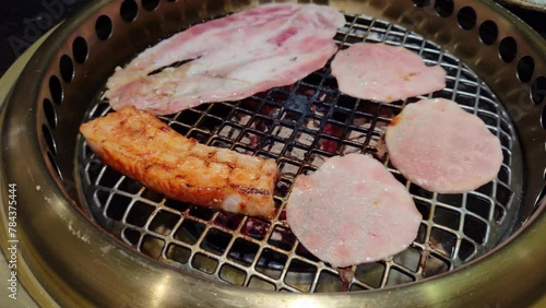 Closeup pork belly strips and beef pieces on metal grill with beef on Japanese Yakiniku style photo