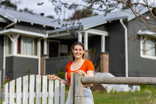 young female homeowner standing smiling at the gate of her home photo