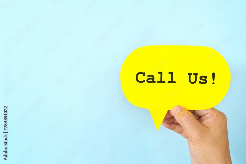 Human hand holding speech bubble with written phrase Call Us or Contact Us.