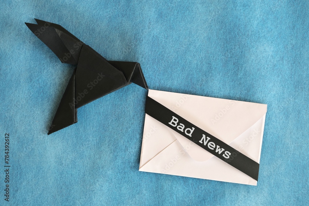 Black raven paper origami carrying white envelope letter with word Bad News. Deliver and bearer of bad news concept.