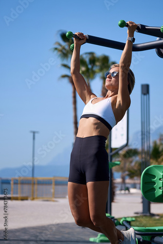 Young fit woman doing a pull up workout in the playground. 
