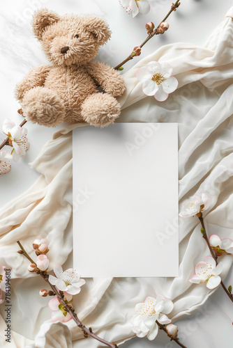 High-angle view of a plush teddy bear beside a blank card and cherry blossoms, ideal for invitations.