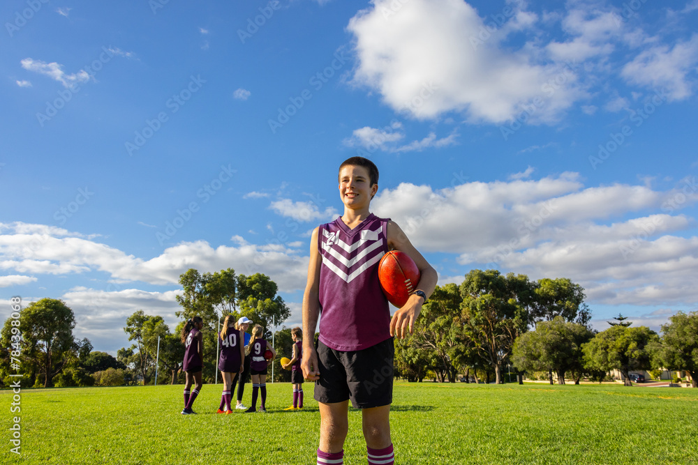 © Austockphoto - one boy in football uniform standing in front of his teammates holding a football
