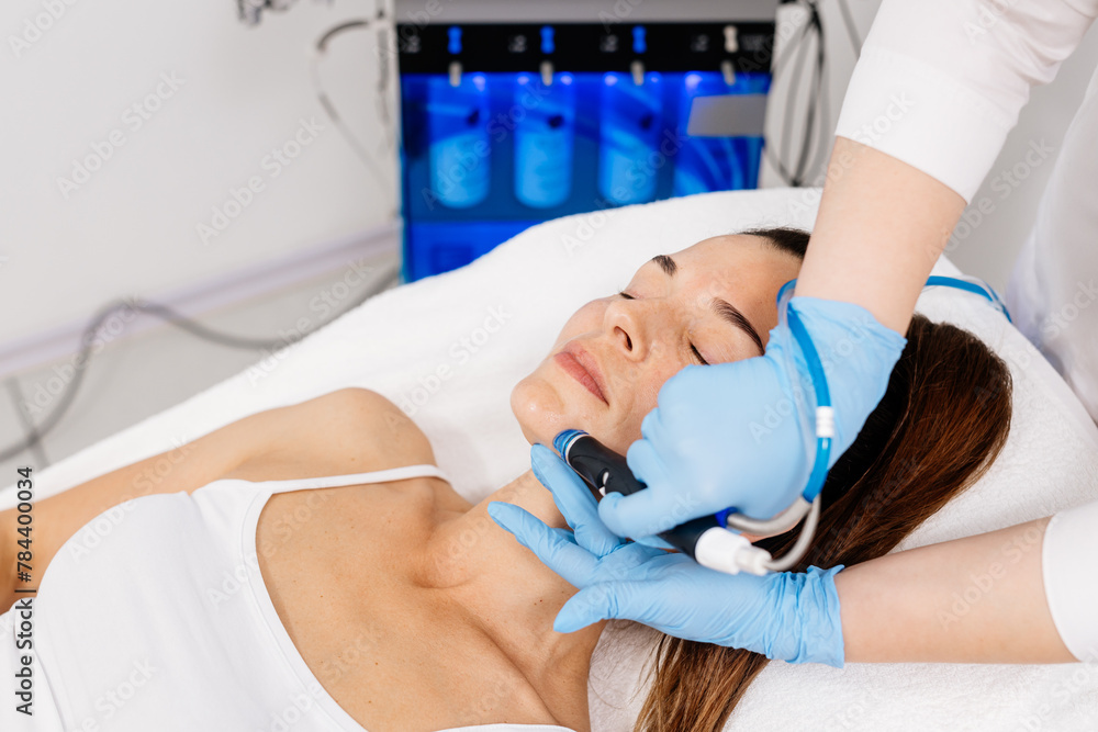Obraz premium Close-up of a cosmetologist's hands polishing and cleansing the skin of a middle-aged woman's face using a vacuum machine. Concept of skin care, rejuvenation and cosmetology.