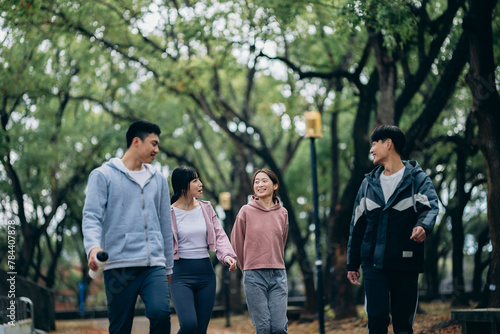 young Asians walk outdoors, sharing their recent exercise experiences as they stroll. They also use reusable water bottles, embodying the concept of sustainable living.