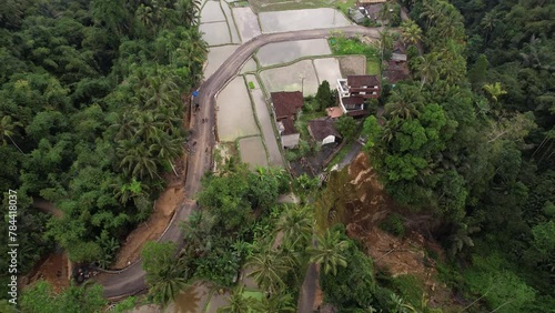 New detour road under construction, roadbed already done across rice fields. Aerial shot, old way destroyed by landslide. Camera fly around at height, showing accident site and roadwork area photo
