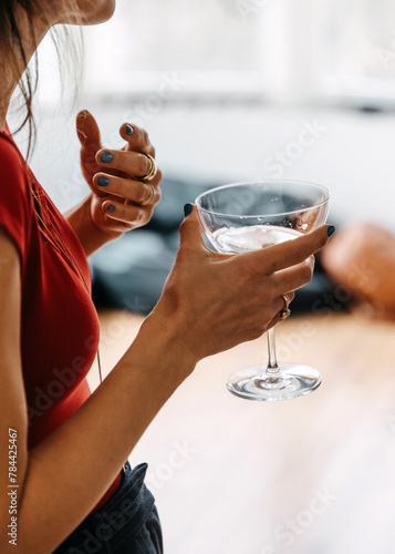 Woman in red with blue nails holding glass, sophisticated gesture.