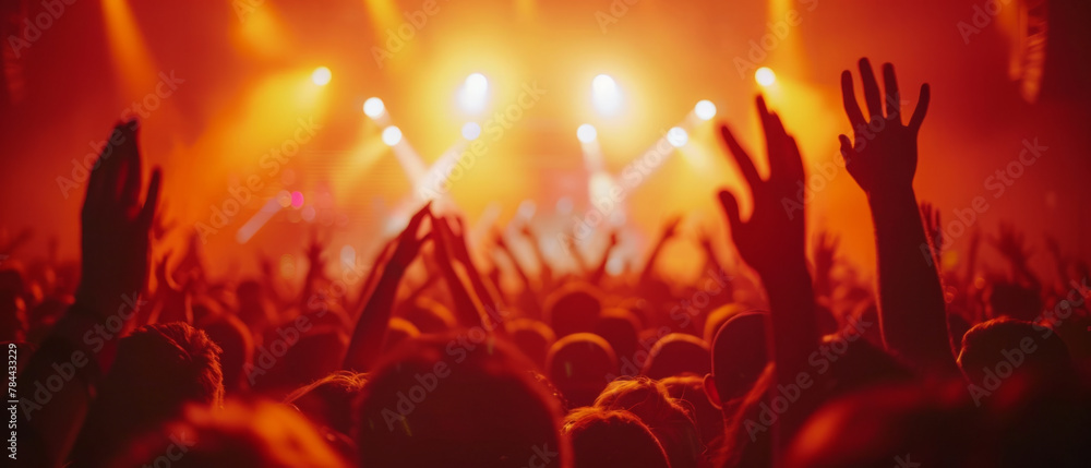 Energetic crowd cheering with hands in air at music festival, in front of stage with colorful lights and sound equipment.