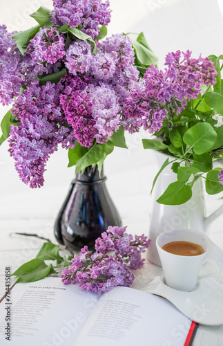 A bouquet of flowers on the window and coffee in a white cup in the rays of sunlight. A bouquet of lilacs and a cup of coffee. 