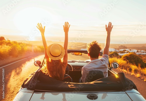 Happy couple driving convertible car on the road - Boyfriend and girlfriend with arms up having fun on a rental auto