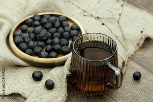 Tea with blueberries on a wooden background. A cup of tea with blueberries, berries, tree branches with swollen buds create a spring mood.