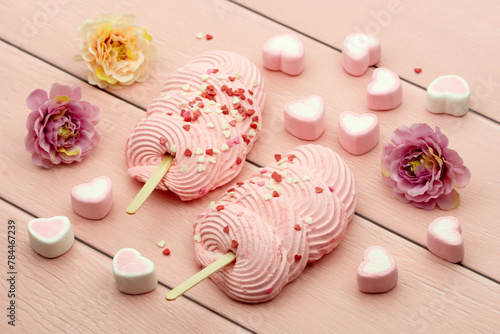 Dessert on a pink background. Two marshmallow popsicle cakes. Pink marshmallow hearts are scattered on a pink wooden background. Poster for interior.