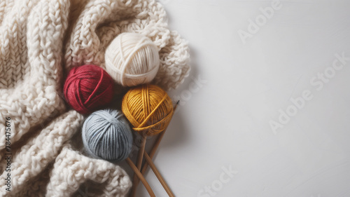 Colorful yarn balls with knitting needles and a knitted blanket on white background.