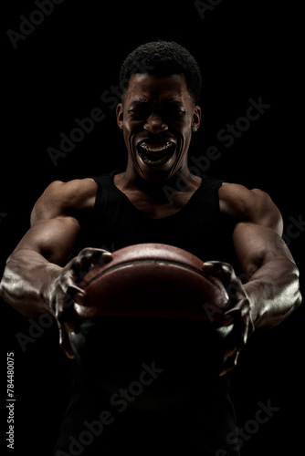 Basketball player holding a ball against black background. Screaming african american man silhouette. © Nikola Spasenoski