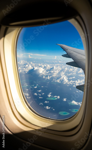 Wing view from a plane with blue sky and low clouds, flying into the Maldives, Indian Ocean.