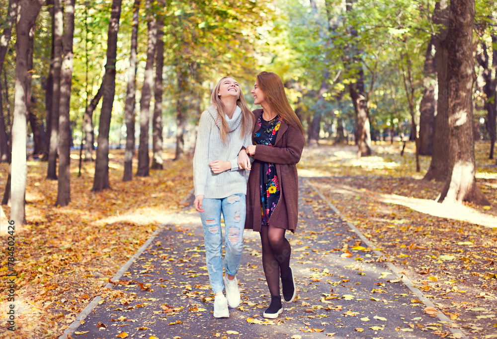 Fototapeta premium Fashionable beautiful young girlfriends walking together in the autumn park background. Having fun and posing.
