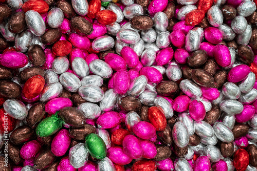 A lot of candies for background. Colorful chocolate easter eggs. Pile or group of multi colored colourful foil wrapped chocolate easter eggs in pink, red, silver, brown and green colors.
