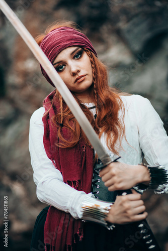 Outdoor portrait of young female in pirate costume holding a sword.