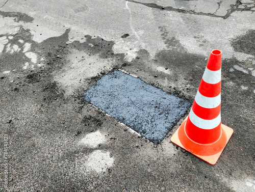 Red and white cone next to hole in Asphalt road surface