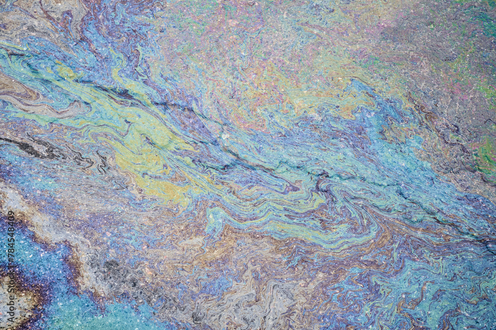 Colorful petrol oil spill creating a textured surface on the wet pavement