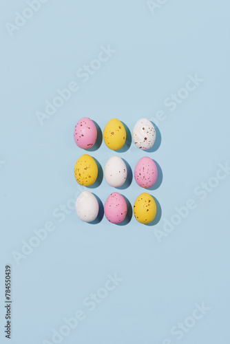 Pattern of chocolate Easter eggs in pink, white and yellow colors on a blue background. Creative Easter concept