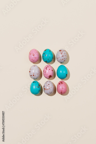 Pattern of chocolate Easter eggs in pink, beige and blue colors on a beige background. Creative Easter concept