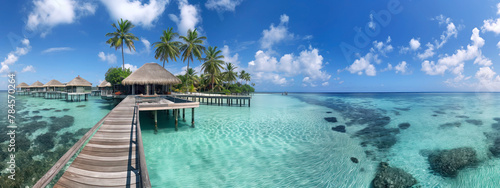 Panoramic view of a tropical resort with overwater bungalows. A wooden walkway leads to thatched-roof huts amidst clear blue waters and palm trees under a sunny sky © Denniro