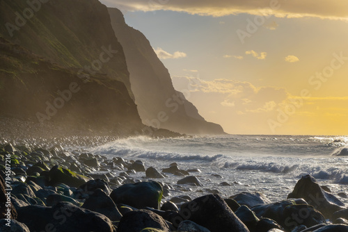 Volcanic rock cliffs Achadas da Cruz in backlit sunlight. Waves of the Atlantic Ocean. Beautiful sunset seascape of the resort island of Madeira, Portugal