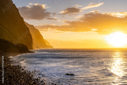 Volcanic rock cliffs Achadas da Cruz in backlit sunlight. Waves of the Atlantic Ocean. Beautiful sunset seascape of the resort island of Madeira, Portugal