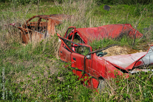 Rusty and broken red abandoned car in the outdoors. Old abandoned rusty car without wheels on the side of the road	
