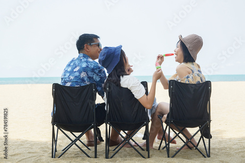 Parents and daughter have fun eating ice cream on portable chairs at the beach.