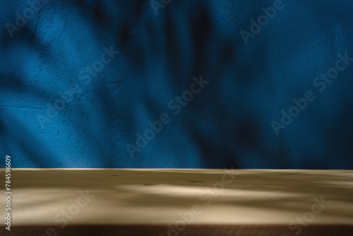 Empty table on dark blue wall background. Minimalist composition with abstract shadow on the wall and light reflections. Mock up for presentation, branding products, cosmetics food or jewelry.	