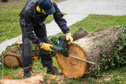 A man in uniform cuts an old tree in the yard with an electric saw