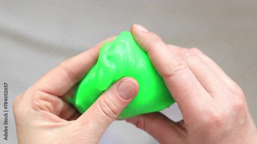 The girl kneads green slime. Female hands stretching bright green slime close-up, top view. Anti-stress toy for relaxation. A fun sensory activity. Toy store concept The girl kneads green slime. Female hands stretching bright green slime close-up, top view. Anti-stress toy for relaxation. A fun sensory activity. Toy store concept