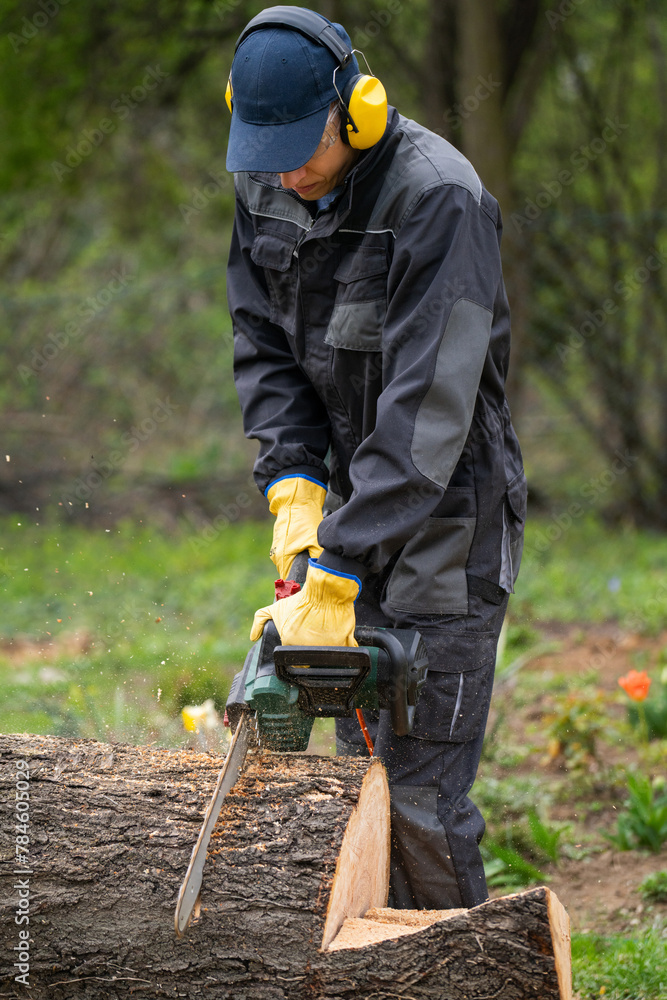 A man in uniform cuts an old tree in the yard with an electric saw A man in uniform cuts an old tree in the yard with an electric saw