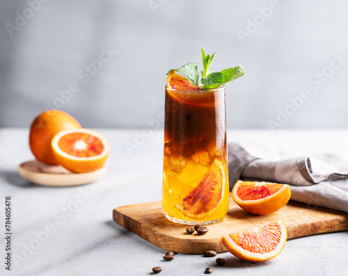 Coffee with orange juice (bumble) in a tall glass with ice and mint on a wooden board on a light background