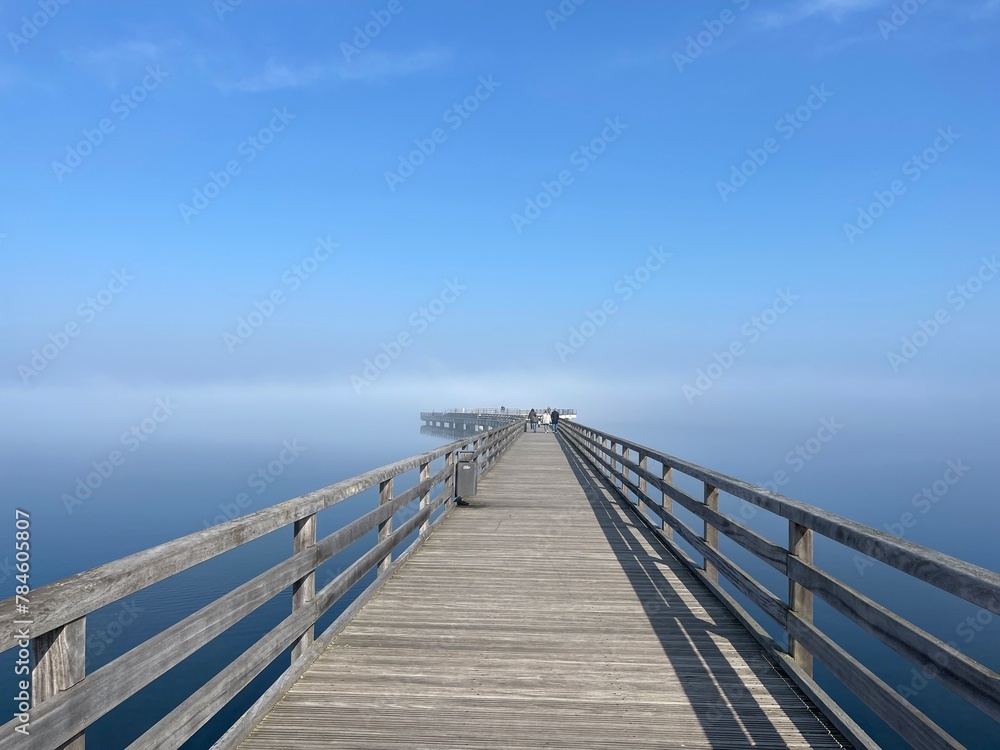 long wooden bridge over the sea in morning fog with sunshine