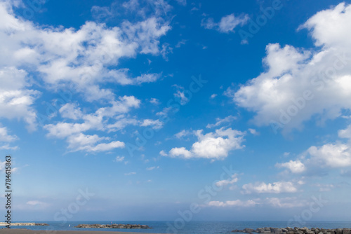 Fototapeta Naklejka Na Ścianę i Meble -  White fluffy cumulus clouds against a blue sky with haze above a body of water