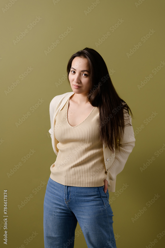Brunette asian woman in cardigan and jeans looking at camera isolated on green, body positive concept Brunette asian woman in cardigan and jeans looking at camera isolated on green, body positive concept