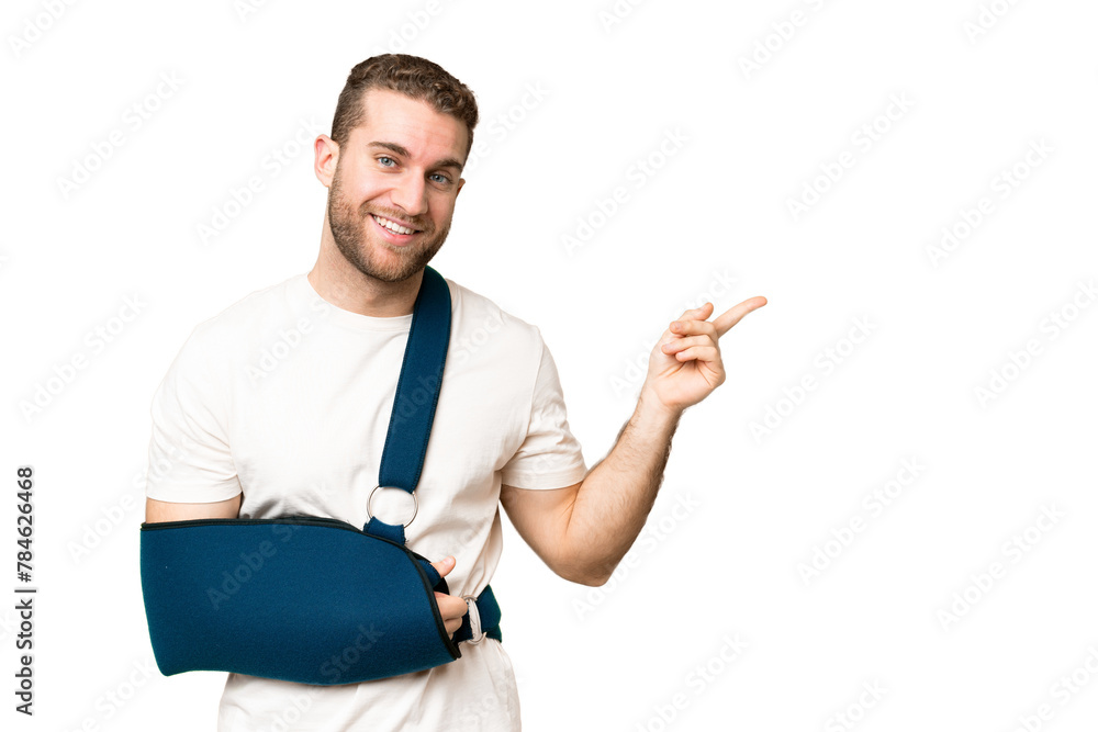 Young handsome blonde man with broken arm and wearing a sling over isolated chroma key background pointing finger to the side Young handsome blonde man with broken arm and wearing a sling over isolated chroma key background pointing finger to the side