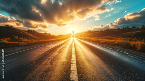 Silhouette of a person standing in the middle of an empty road at sunset. Dramatic sky and sun rays over rural landscape. Inspirational journey and life goals concept with copy space photo