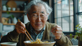 Elderly man eating noodles with chopsticks.