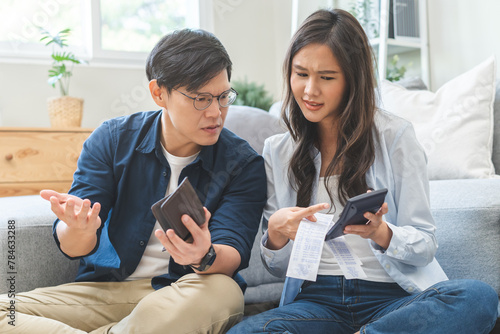 Stressed financial owe asian young couple love sitting stressed and confused by hand hold wallet calculate expense from invoice , no money to pay, mortgage or loan. Debt, bankrupt or bankruptcy people